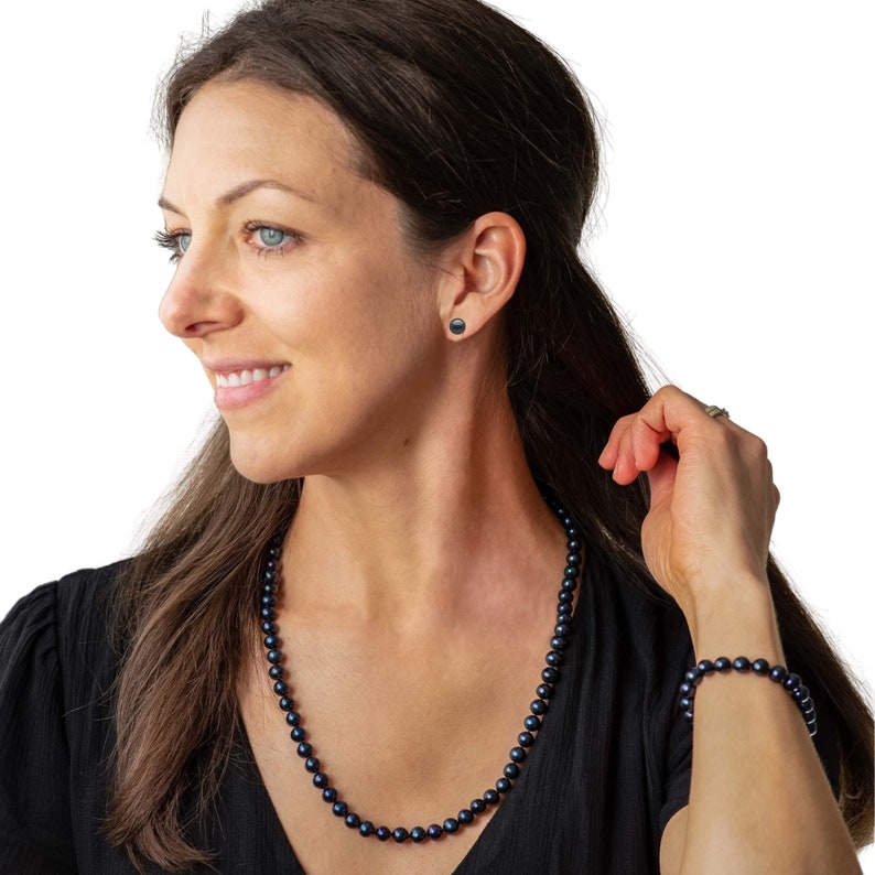 May include: A woman wearing a black pearl necklace, matching bracelet, and stud earrings. The jewelry is a deep, iridescent black color. The woman is wearing a black top.