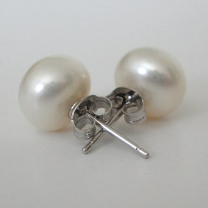 May include: A pair of white pearl stud earrings. The pearls are round and have a lustrous sheen. The earring posts and backs are made of silver-colored metal.