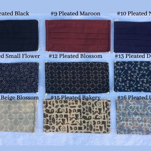 May include: A collection of pleated face masks in various colors and patterns. The masks include solid colors like black, maroon, and navy blue, and patterned designs such as small flowers, blossoms, dragonflies, and a bakery theme. Each mask has white elastic ear loops.