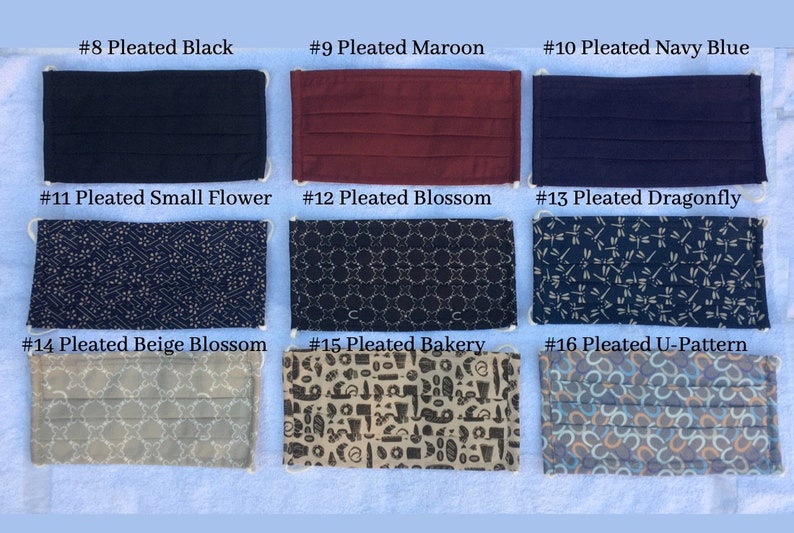May include: A collection of pleated face masks in various colors and patterns. The masks include solid colors like black, maroon, and navy blue, and patterned designs such as small flowers, blossoms, dragonflies, and a bakery theme. Each mask has white elastic ear loops.