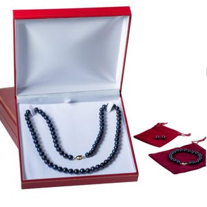May include: A red jewelry box with a white interior holds a dark blue pearl necklace. A matching bracelet and earrings are displayed in separate red velvet pouches. The necklace has a gold clasp.