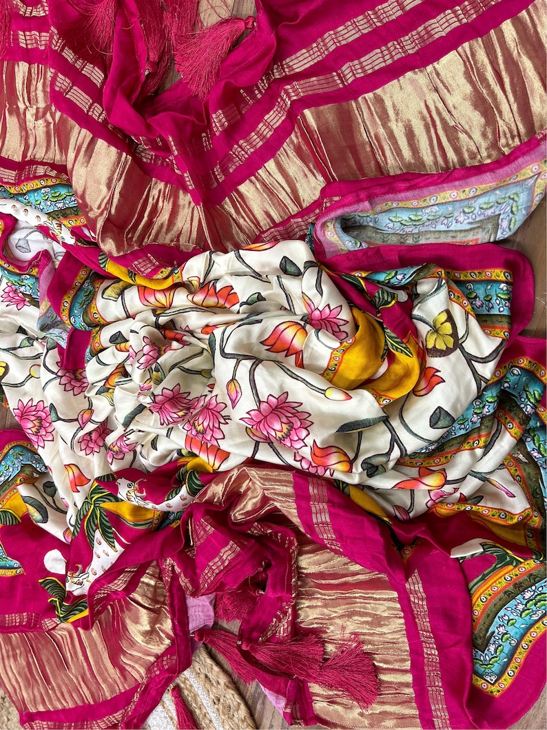 May include: A white and yellow floral patterned fabric with pink flowers and green leaves. The fabric is folded and draped over a pink and gold fabric with a fringe.