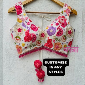 Pode incluir: Top branco bordado com desenhos florais rosa e multicoloridos. O top tem um decote em V e é decorado com contas rosa. O texto "CUSTOMISE IN ANY STYLES" é visível na imagem.