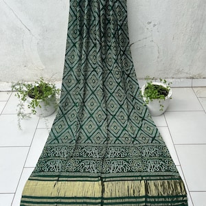 Pode incluir: Um sari de seda verde e dourado com uma borda de elefantes e uma guarnição dourada. O sari tem uma franja na parte inferior.