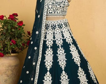 May include: A teal green lehenga with white embroidery. The lehenga has a matching crop top with a white embroidered design. The outfit is decorated with white beads and sequins.