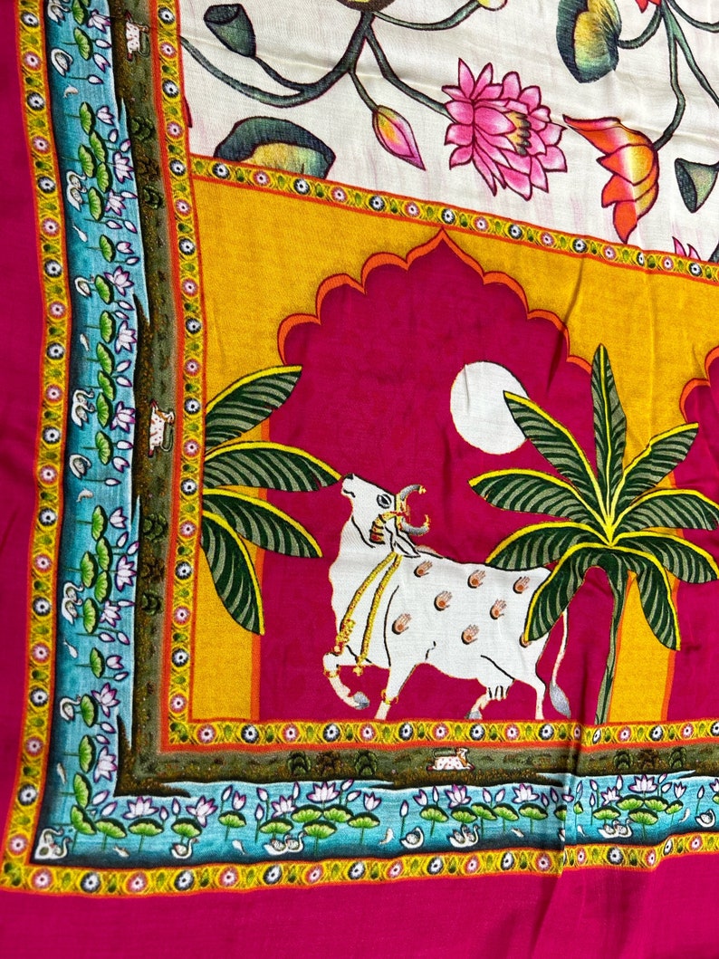 May include: A pink fabric with a colorful design featuring a white cow, palm trees, and a moon. The design is framed by a yellow, orange, and blue border with floral motifs.