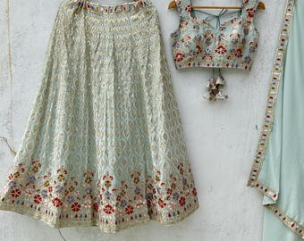 May include: A light blue embroidered skirt with a matching embroidered top and a light blue dupatta. The skirt and top feature floral embroidery with gold accents. The dupatta has a gold border with mirror work.