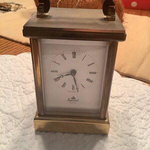 May include: A brass mantel clock with a white face and black Roman numeral hour markers. The clock has a black handle and says "Imperial Quartz" on the face.