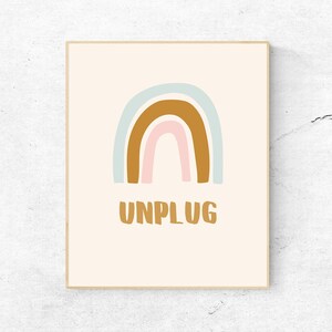 May include: A framed print with a rainbow design in shades of blue, brown, and pink. The text "UNPLUG" is written in brown below the rainbow.