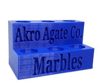 May include: Blue plastic marble holder with the text "Akro Agate Co. Marbles" on the front.