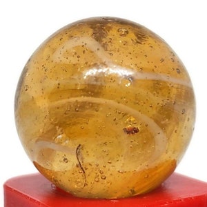 May include: A clear glass marble with a swirl of white and brown. The marble has a textured surface with small air bubbles.