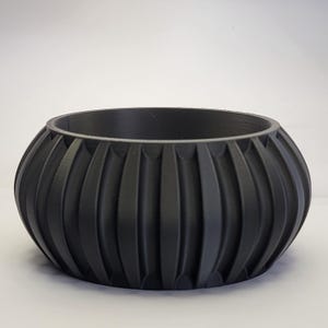 May include: A black, round planter with a ribbed design. The planter is made of a smooth, matte material.