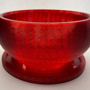 May include: A vibrant red bowl with a rounded body and a wide, flat base. The bowl has a smooth, glossy finish and a textured appearance. The design is simple and elegant, suitable for various uses.