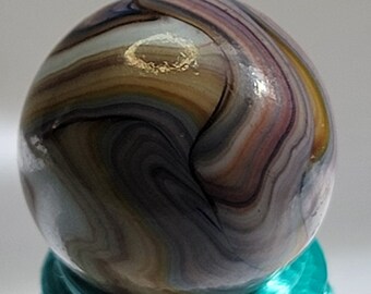 May include: A colorful glass marble with swirling patterns of brown, purple, and white. The marble has a gold fleck on the surface.