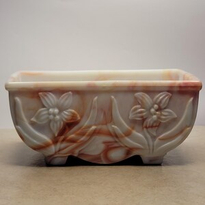 May include: A white and orange marbled glass planter with a rectangular shape and carved floral details. The planter has four small feet.