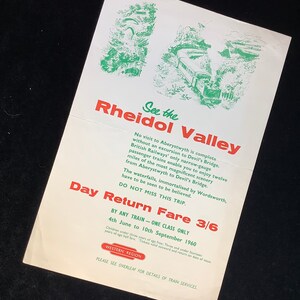 May include: A vintage travel poster advertising a day return trip on the Rheidol Valley Railway in Wales. The poster features a green illustration of a train traveling through a lush valley. The text reads "See the Rheidol Valley" and "Day Return Fare 3/6".