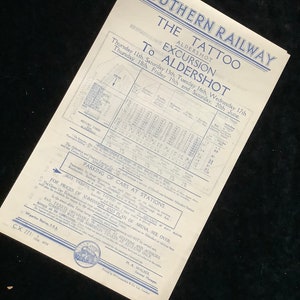May include: A vintage Southern Railway poster advertising an excursion to the Aldershot Tattoo. The poster features a timetable with departure times and fares from various stations to Aldershot. The poster also includes information about parking and ticket prices for the Tattoo.