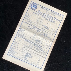 May include: A vintage train timetable from the Great Western Railway (GWR) for half-day excursions in August 1938. The timetable lists destinations including Barry, Penarth, Bristol, Port Talbot, Neath, Swansea, and the Wye Valley. It includes departure times and fares for different classes.
