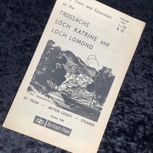 Pode incluir: Brochura de viagem vintage para passeios de um dia a Trossachs, Loch Katrine e Loch Lomond. A brochura apresenta uma ilustração a preto e branco de uma paisagem com montanhas e árvores. Inclui o texto "British Rail" e "Época 1966".