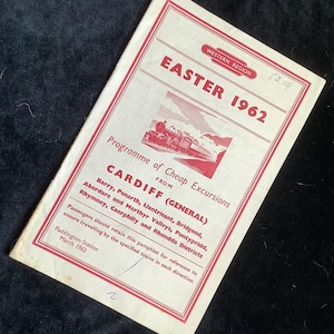 May include: Vintage Easter 1962 pamphlet from the Western Region, featuring a red and white design. The cover includes text about cheap excursions from Cardiff, with a train illustration. The pamphlet is slightly worn.