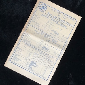 May include: A vintage train timetable for half-day excursions in the Barry and Penarth districts of Wales. The timetable lists destinations, dates, and fares for trips to Bristol, Port Talbot, Neath, Swansea, and the Wye Valley. The timetable is printed on a cream-colored paper with blue text and a GWR logo in the top right corner.