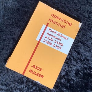 May include: An orange operating manual for British Railways locomotives. The cover features the text "operating manual" in red, along with details about the locomotives, including model numbers. The bottom of the cover reads "AEI SULZER".