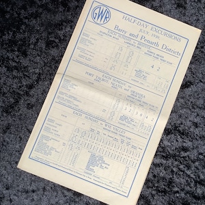 May include: A vintage Great Western Railway (GWR) timetable for half-day excursions in July 1939. The timetable lists train schedules for trips from Barry and Penarth to Bristol, Port Talbot, Neath, Swansea, and the Wye Valley. The timetable includes departure times, arrival times, and return fares.