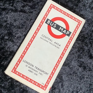 Puede incluir: Un mapa de autobuses vintage de 1959 de London Transport para el área central, incluidos los trolebuses. La cubierta rectangular de papel presenta un logotipo circular rojo, texto negro y un borde decorativo con símbolos rojos y blancos sobre un fondo crema.