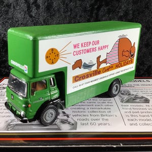 May include: A green and white Crosville Holidays truck model. The truck features the text "WE KEEP OUR CUSTOMERS HAPPY" and a cartoon figure. The model is a replica of a vehicle from Britain's roads.