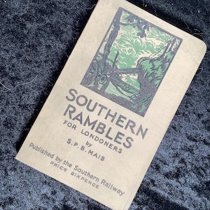 May include: A vintage book titled "SOUTHERN RAMBLES FOR LONDONERS" by S.P.B. MAIS. The cover features a green and black illustration of a landscape scene. The book is a light tan color and is set against a dark blue textured background.