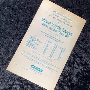 Pode incluir: Um bilhete vintage da British Rail para uma excursão especial ao Museu de Transportes Britânico, datado de 11 de abril de 1965. O bilhete creme apresenta texto a preto e azul com horários de partida e chegada e tarifas incluídas. O bilhete é para Clapham High Street, Londres.