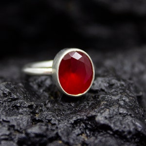 Può includere: Un anello d'argento con una pietra ovale rossa. L'anello è su uno sfondo nero.