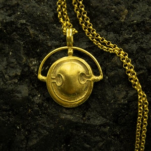 Puede incluir: Un collar de oro con un colgante redondo y adornado con un dise&ntilde;o estilizado. El colgante est&aacute; suspendido de una delicada cadena de oro.