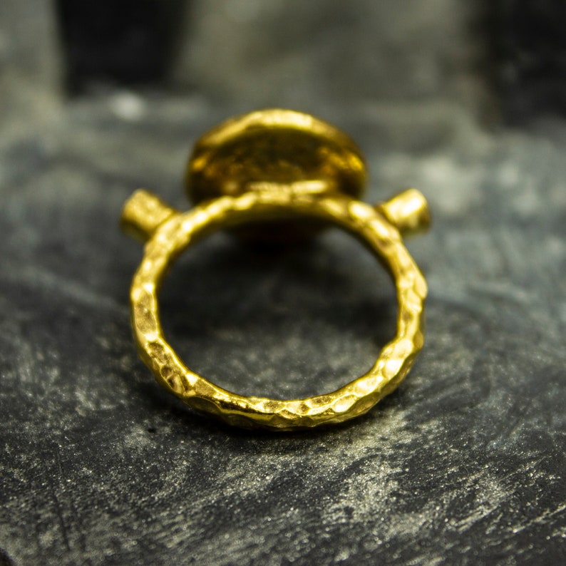 Puede incluir: Un anillo de oro con una banda texturizada y una parte superior redonda y martillada de oro.