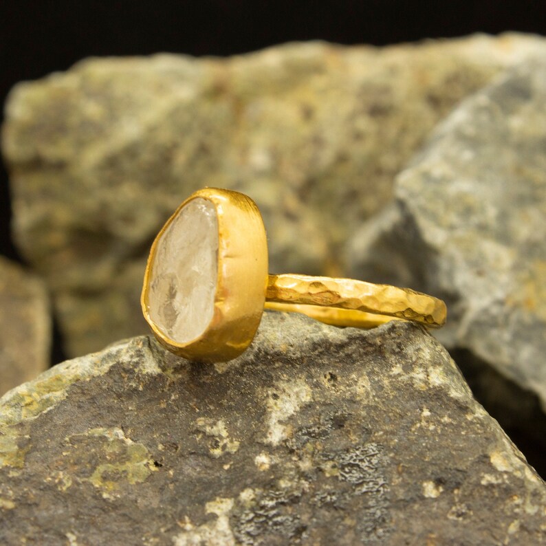 May include: A gold ring with a clear, faceted gemstone. The ring band is hammered and has a textured finish.