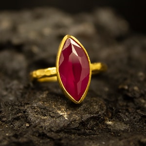 Può includere: Un anello d'oro con una grande pietra preziosa di rubino di forma a marquise sfaccettata.