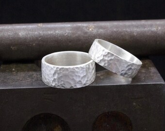 May include: Two silver hammered wedding bands. The bands are thick and have a textured surface.