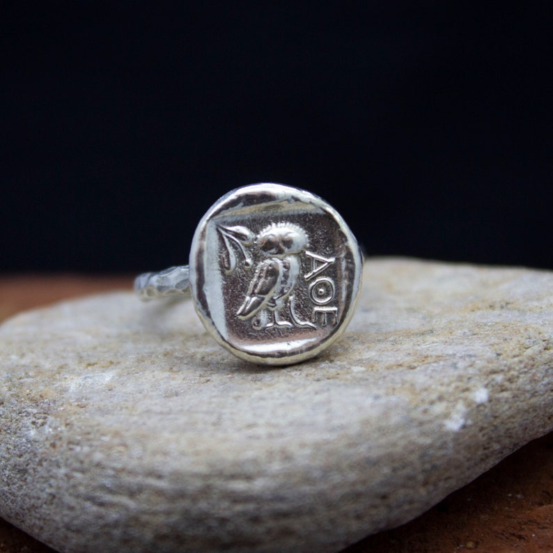 May include: Silver ring with a raised design of an owl and the letters "AOE".