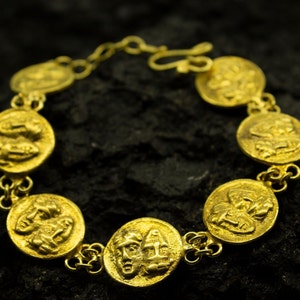 May include: A gold bracelet with a chain and round medallions featuring embossed faces.
