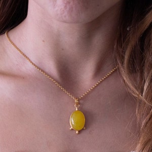 May include: A gold chain necklace with a yellow oval pendant. The pendant has a gold setting with three small gold balls on the bottom.