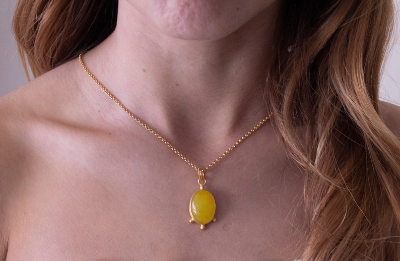 May include: A gold chain necklace with a yellow oval pendant. The pendant has a gold setting with three small gold balls on the bottom.