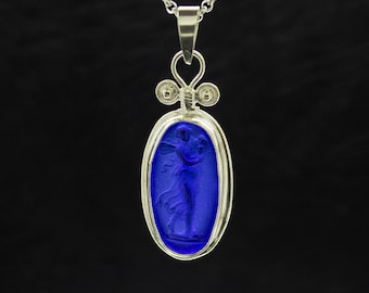 May include: A silver chain necklace with a blue glass pendant featuring a carved image of a woman. The pendant is oval shaped and has a silver frame.