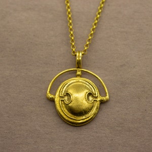 Puede incluir: Un collar de oro con un colgante redondo que presenta un dise&ntilde;o estilizado. El colgante est&aacute; suspendido de una cadena delicada.