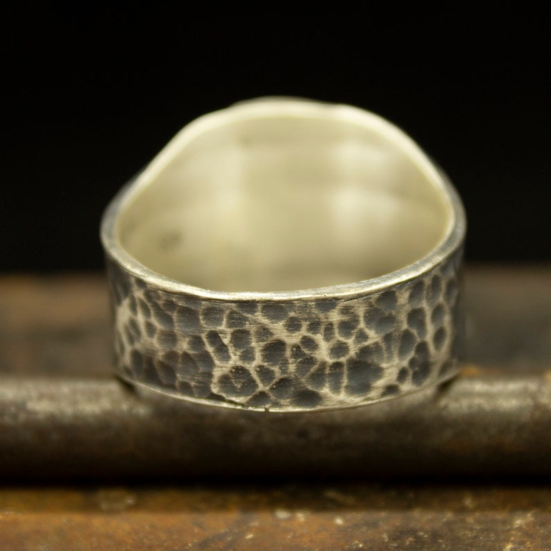 May include: A silver ring with a hammered texture on the band. The ring is wide and has a rounded shape.
