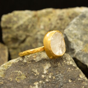 May include: A gold ring with a clear, faceted gemstone. The ring band is hammered and has a textured finish.