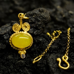 Puede incluir: Un collar de oro con un colgante de piedra amarilla. El colgante tiene un diseño detallado con una pequeña piedra transparente en la parte inferior.