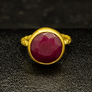 May include: A gold ring featuring a large, oval-shaped, deep red gemstone.