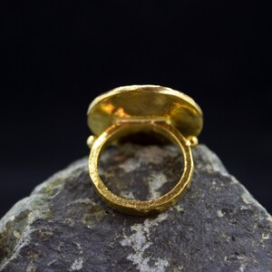 Peut inclure: Une bague en or avec un dessus rond, plat et large. La bague est pos&eacute;e sur une roche grise.