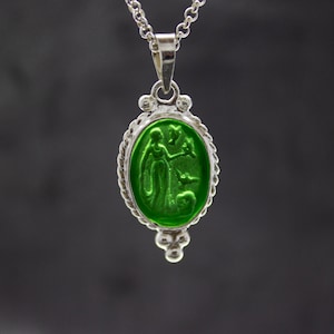 Puede incluir: Un collar de cadena de plata con un colgante de vidrio verde que presenta una imagen tallada de una mujer con un p&aacute;jaro.