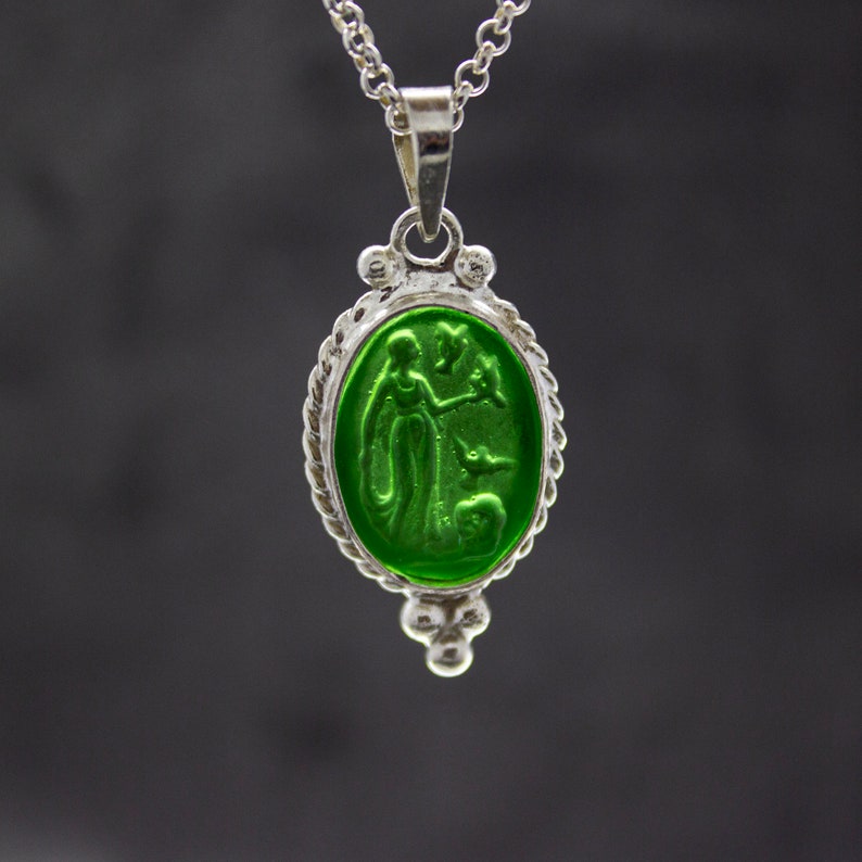 Puede incluir: Un collar de cadena de plata con un colgante de vidrio verde que presenta una imagen tallada de una mujer con un p&aacute;jaro.